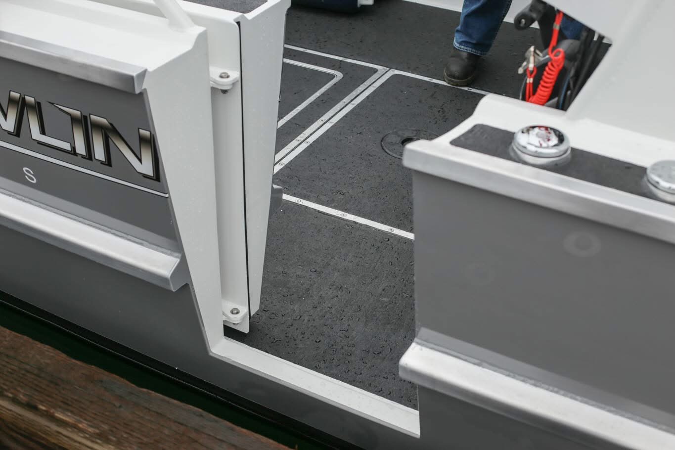 Kwigwis Adventures boat boarding area with white railings and black anti-slip deck surface, featuring storage compartments and safety equipment mounted on the white interior walls.